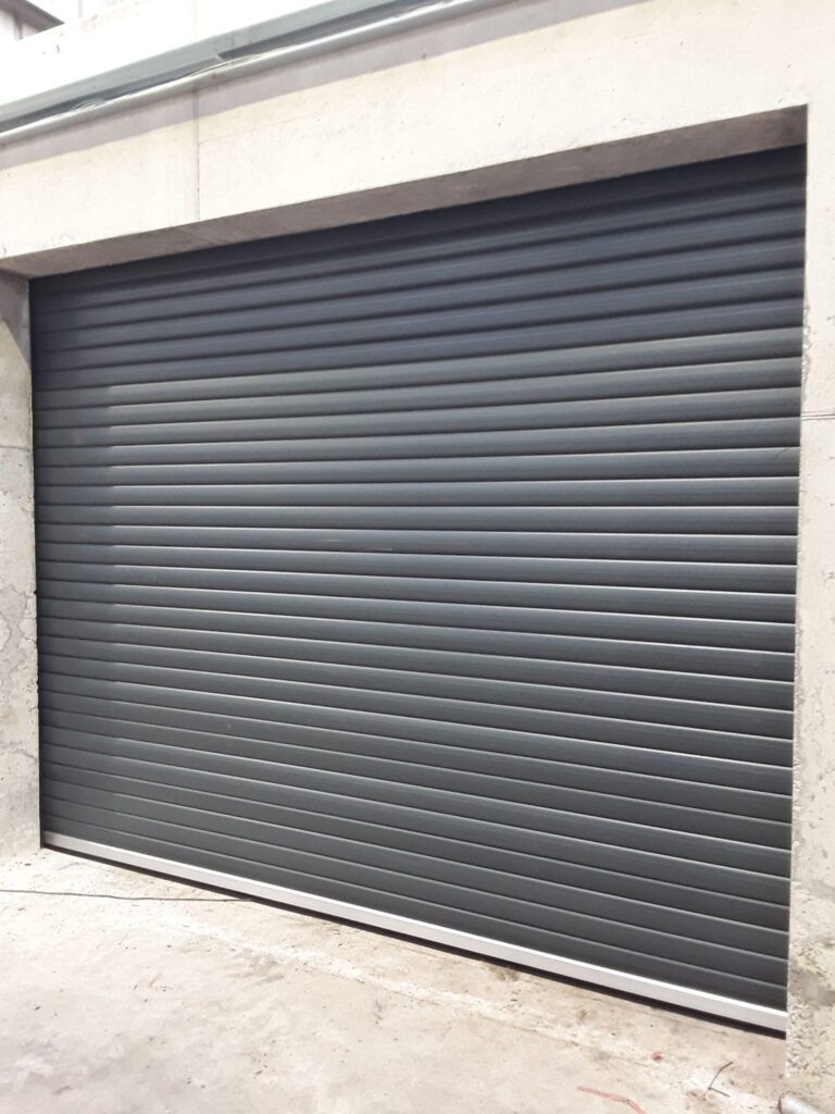 Black metal roller shutter door closed on a concrete garage entrance.