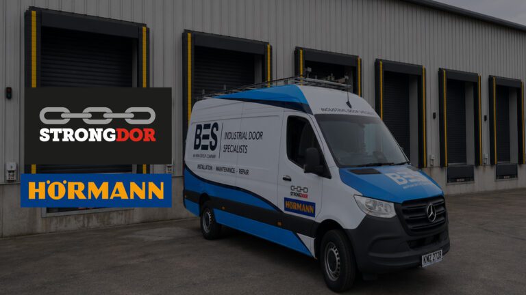 A white and blue BES Industrial Door Specialists van is parked in front of a row of industrial loading bays with Strongdor and Hörmann logos visible.